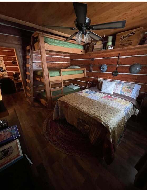 Log cabin themed room with stacked bunk beds, queen bed, and vintage Domino crate decor