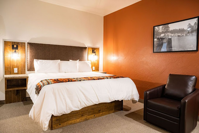King room with warm orange accent wall, leather armchair, and historic Cloudcroft photograph