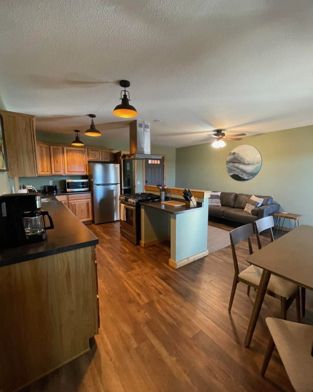 Open-plan kitchen, dining area, and living room at Osha Trail Lodging with hickory cabinets, stainless appliances, mid-century furniture, and a circular mountain print