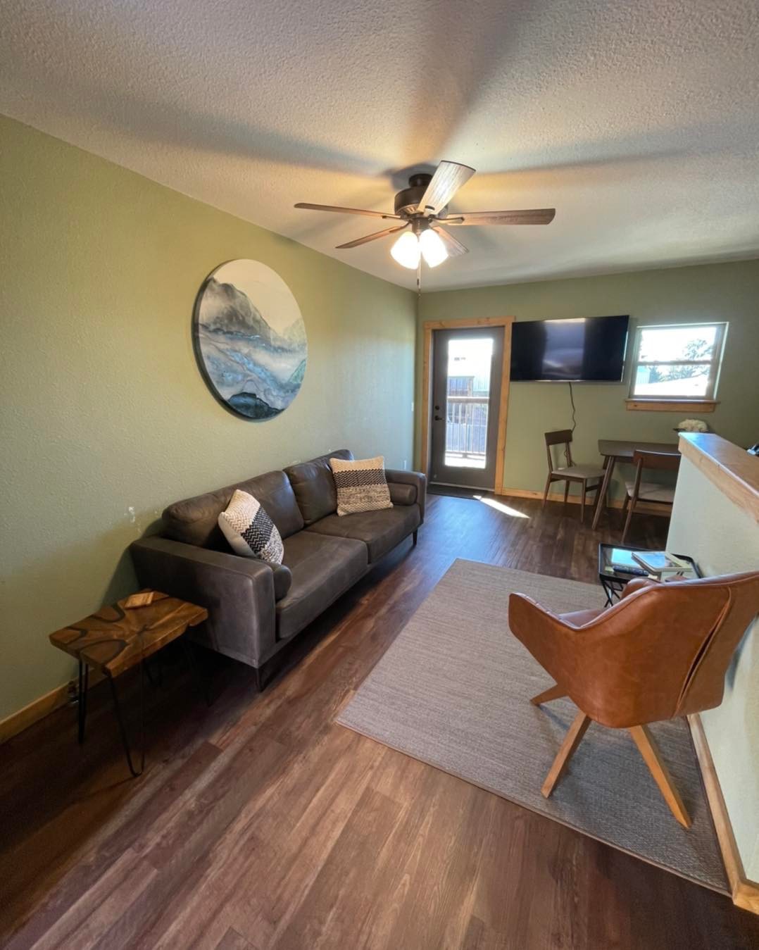 Living room at Osha Trail Lodging with brown leather sofa, leather chair, mountain print, ceiling fan, and a wall-mounted TV