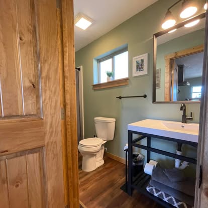 Bathroom at Osha Trail Lodging with sage-green walls, modern vanity with steel base, framed art, and a small window