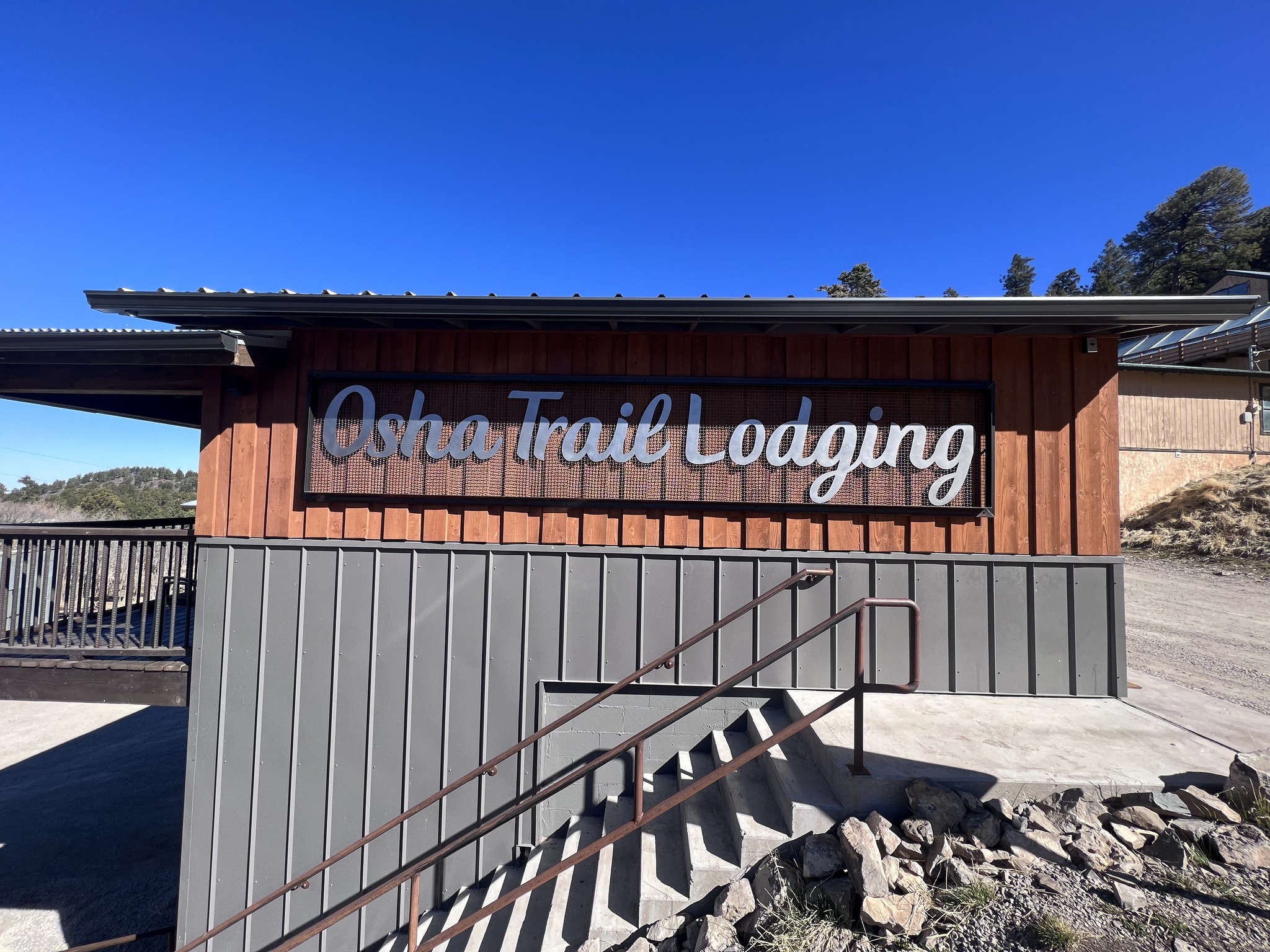 Carved Osha Trail Lodging sign on the building exterior with vertical wood siding and a clear blue sky