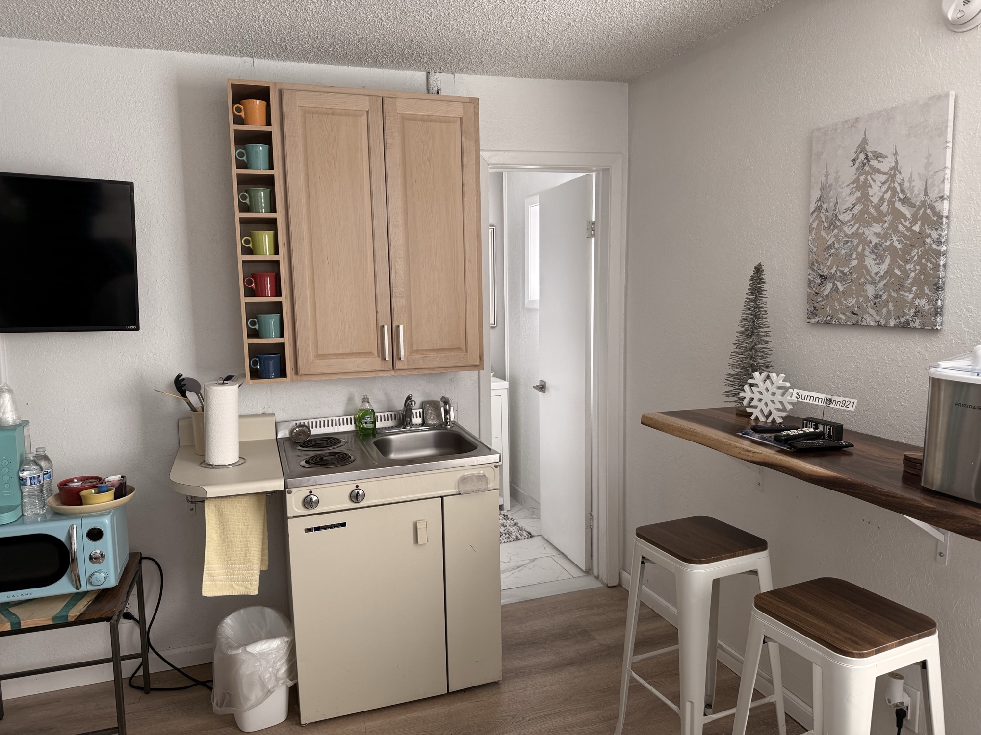 In-room kitchenette at The Summit Inn with mint microwave, colorful coffee mugs on a built-in shelf, vintage stove, and counter stools